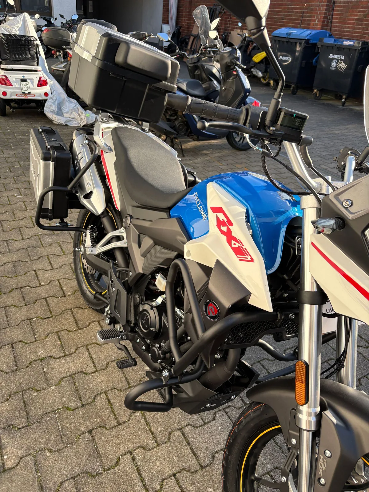 Reiseenduro in Weiß, Blau und Rot mit Koffern auf dem Hof der Werkstatt