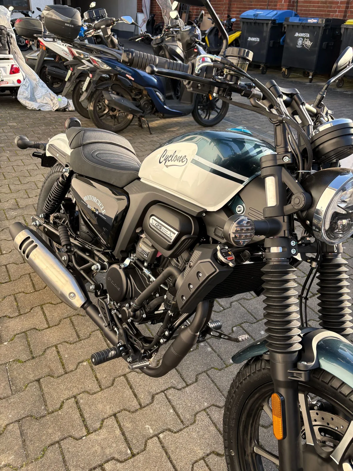 Motorrad im Retro-Stil mit hellem Tank und Chromauspuff auf dem Hof
