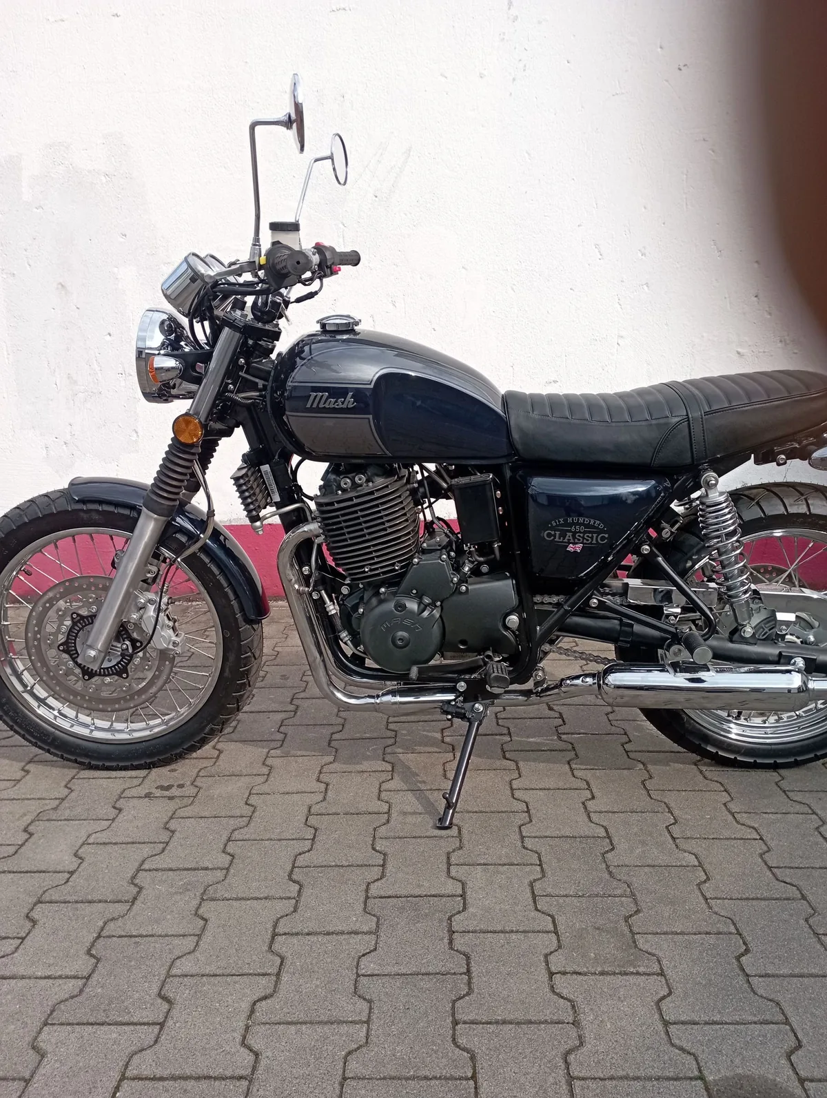 Schwarzes Retro-Motorrad mit Speichenrädern vor heller Hauswand